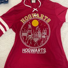 a red shirt with hogwarts on it sitting on top of a white blanket