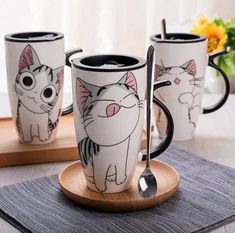 three coffee mugs with cartoon cats on them sitting on a wooden tray next to flowers