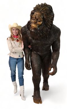 a woman standing next to a statue of a bigfoot with a cowboy hat on