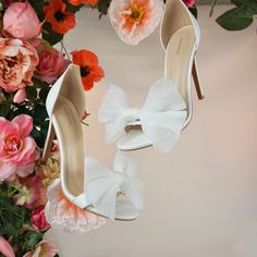 two pairs of white high heel shoes with bows and flowers in the background on display