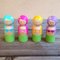 five wooden dolls are lined up on a wood table, painted in different colors and sizes