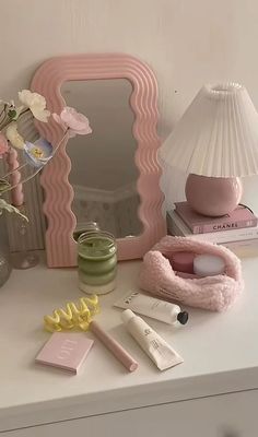 a white dresser topped with lots of pink items next to a mirror and vase filled with flowers