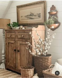 an old dresser with baskets and flowers in it next to a painting on the wall