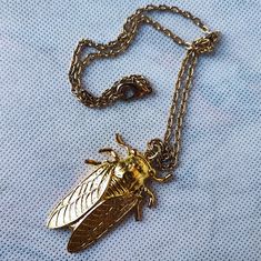 a necklace with a bee on it sitting on top of a blue cloth next to a chain