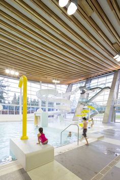 two children are playing in the water at an indoor swimming pool that is surrounded by large windows