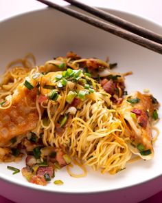 a white plate topped with noodles and meat next to chopsticks on a table