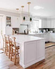 a large kitchen with white cabinets and wooden flooring, along with an island in the middle