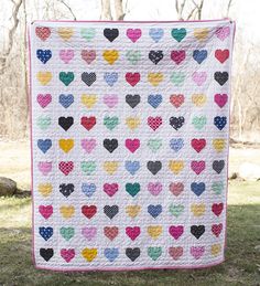 a heart quilt hanging on the side of a tree in front of some trees and grass