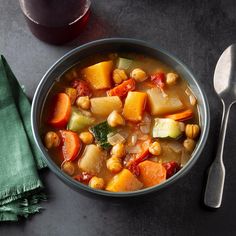 a bowl of stew with carrots, potatoes and spinach next to a glass of wine