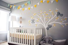 a baby's room decorated in yellow and gray with an elephant tree mural on the wall