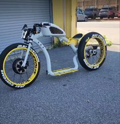 a white and yellow motorized bike parked in front of a garage with two tires on it