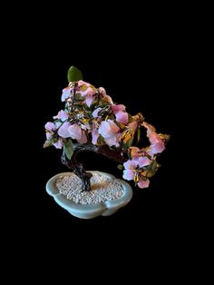 a bonsai tree with pink flowers on top of a white rock in front of a black background