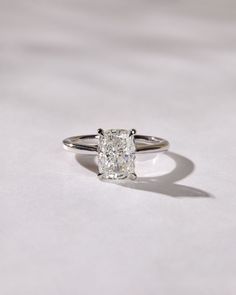 an engagement ring with a cushion cut diamond in the center, on a white surface