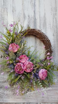 a wreath with pink flowers and greenery is hanging on a white wooden door frame