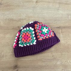 a purple crocheted hat with flowers on it sitting on a wooden floor next to a pair of scissors