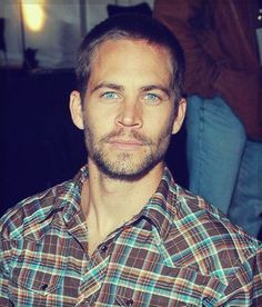 a close up of a person wearing a plaid shirt and looking at the camera with a serious look on his face