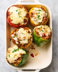 four stuffed peppers in a casserole dish with cheese on top and seasoning