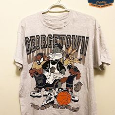 Vintage Ncaa Georgetown Hoyas Looney Tunes T-Shirt, Georgetown Hoyas Shirt, Georgetown University Shirt, Unisex Shirt, Vintage Shirt Our Classic T-Shirt Serves As The Perfect Short-Sleeved Shirt For Your Unique, Funny, Or Personalized Designs. Brand: Gildan Heavy Weight Fabric Classic Unisex Makes This An Easy Fit Size Up If You Want Something Roomier Our Shirts Materials: 100% Cotton ** Note: - Double Check Your Address Before Ordering. - If You Want To Return The Goods, You Are The One To Pay Retro Gray Graphic Print Top, Character Print Crew Neck Top For College, Retro Gray Top With Graphic Print, Sporty Cotton Tops With Cartoon Print, Throwback Short Sleeve Top For College, Throwback Short Sleeve Top, Throwback Cotton Fan Merchandise Tops, Throwback Cotton Tops For Fan Merchandise, Sporty Tops With Character Print For Fans