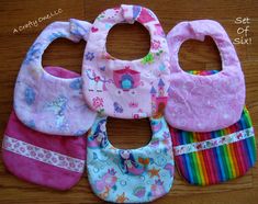 four bibs with different designs on them sitting on a wooden floor next to each other