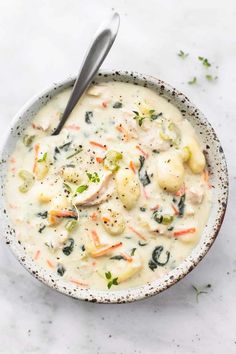 a white bowl filled with soup on top of a marble counter next to a spoon