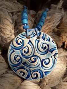 a blue and white ceramic pendant with spirals on it's side hanging from a pile of rope