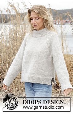 a woman in a white sweater is walking by some tall grass with her hands behind her back