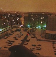 a hand is pointing at the snow covered parking lot in front of some tall buildings