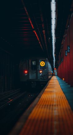 a train is coming down the tracks in a tunnel with red walls and yellow lights