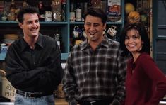 two men and a woman standing in front of a kitchen counter with food on it