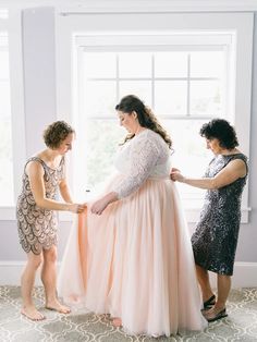 three women standing in front of a window and one is adjusting the dress on another woman