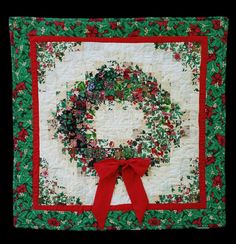 a quilted christmas wreath with red ribbon on the front and green leaves around it