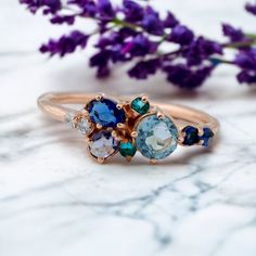 three stone ring sitting on top of a marble table next to purple and green flowers