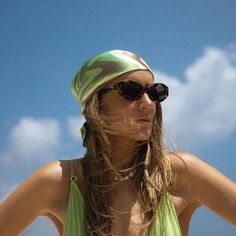 a woman wearing sunglasses and a green tank top with her hair blowing in the wind