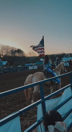 a person riding on the back of a white horse next to an american flag at a rodeo