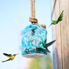 two hummingbirds are flying near a bird feeder that is hanging from a wooden pole