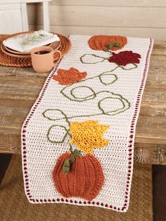 a crocheted table runner with pumpkins and flowers on it sitting on a wooden bench