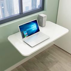 an open laptop computer sitting on top of a white desk in front of a window