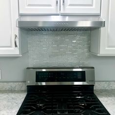 a stainless steel stove top oven in a kitchen with white cabinets and marble counter tops