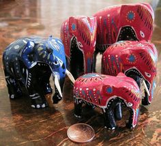 four elephants are painted red, blue and white with designs on them next to a penny