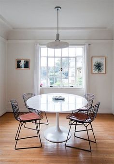 a white table with four chairs around it in front of a window and pictures on the wall