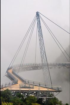 a bridge that is going over some water in the foggy day with trees around it