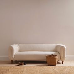 a white couch sitting on top of a hard wood floor next to a wooden basket