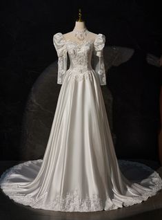 a white wedding dress with long sleeves and lace on the neckline, sitting on a mannequin