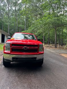 a red truck is parked on the side of the road in front of some trees