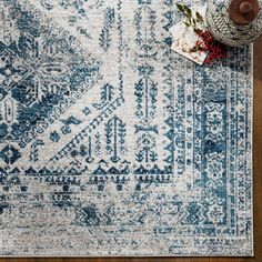 a blue and white rug with an intricate design on the floor next to a vase