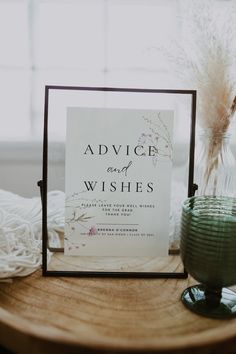 a sign sitting on top of a wooden table next to a vase with flowers in it