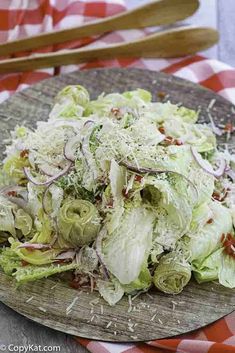 a wooden plate filled with lettuce and onions on top of a checkered table cloth