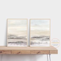 two framed paintings on a shelf next to each other in front of a white wall