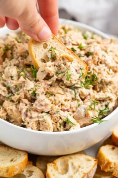 a hand dipping a piece of bread into a bowl of tuna salad