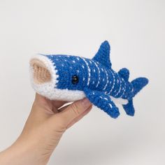 a hand holding a small knitted blue and white toy with a shark on it